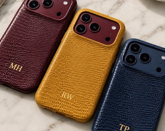Può includere: Tre cover per smartphone con una texture effetto pelle di lucertola in bordeaux, giallo senape e blu navy. Ogni cover presenta un ritaglio per la tripla fotocamera e iniziali impresse in oro: MH sulla bordeaux, RW sulla gialla e TP sulla blu.