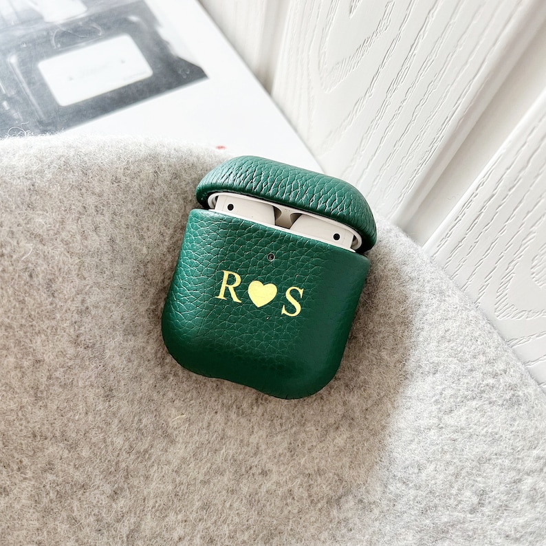 May include: A green leather Airpods case with a gold monogram that reads "R&hearts;S".