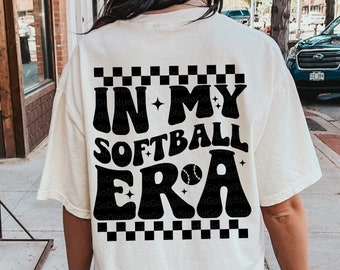 May include: White t-shirt with a black graphic that says "In My Softball Era" with a baseball graphic. The graphic is on a checkered background.