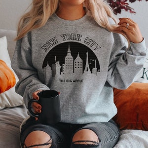 May include: A gray sweatshirt with a black graphic of the New York City skyline and the text "New York City" and "The Big Apple".