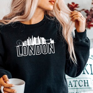 May include: Black sweatshirt with a white graphic of the London skyline and the word "LONDON" underneath.