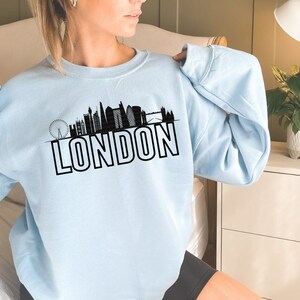 May include: A light blue sweatshirt with a black silhouette of the London skyline and the word "LONDON" in bold black letters.