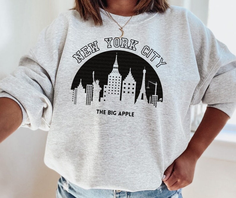 May include: Gray sweatshirt with a black graphic of the New York City skyline and the text "NEW YORK CITY" and "THE BIG APPLE".