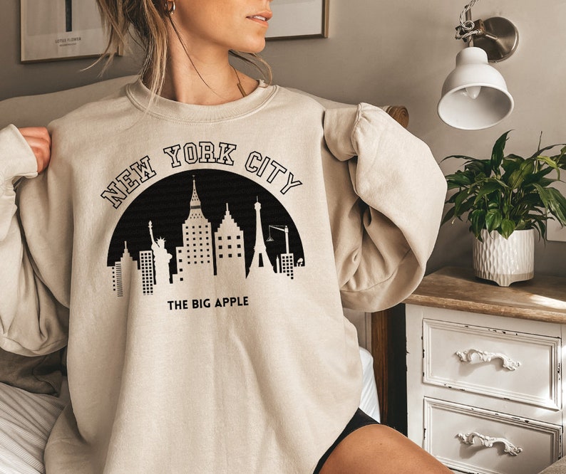 May include: A beige sweatshirt with a black graphic of the New York City skyline and the text "NEW YORK CITY THE BIG APPLE".