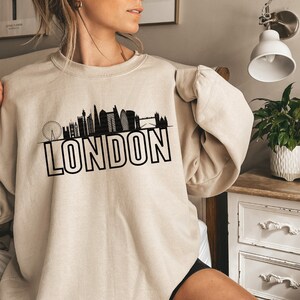 May include: A beige sweatshirt with a black graphic of the London skyline and the word "LONDON" printed in bold black letters.