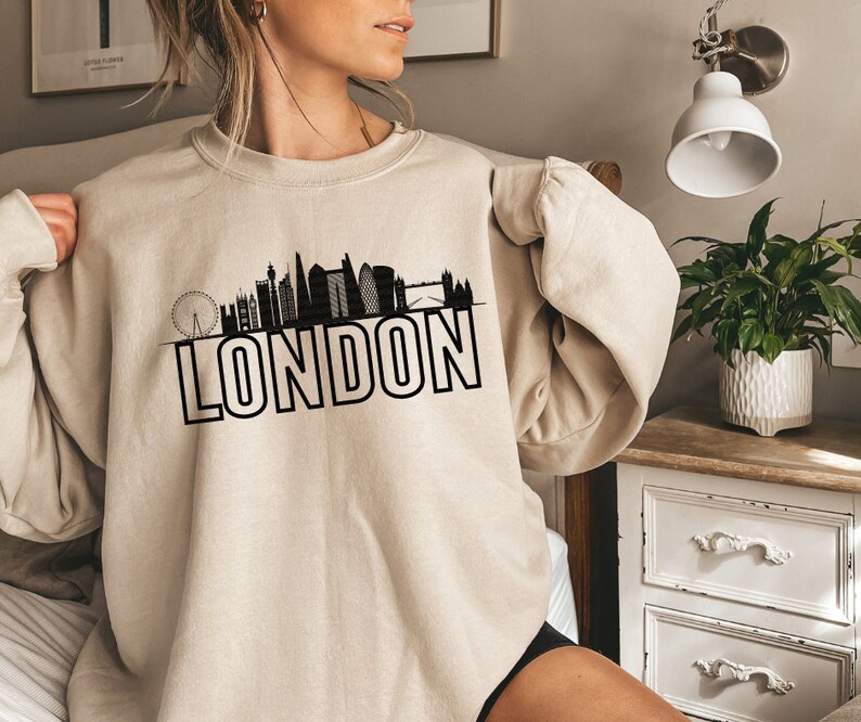May include: A beige sweatshirt with a black graphic of the London skyline and the word "LONDON" printed in bold black letters.