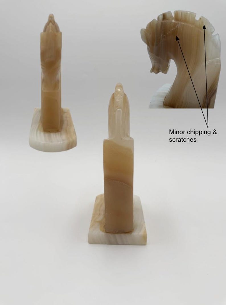 May include: Two onyx sculptures, one a tall, rectangular shape and the other a horse head. The sculptures are beige and cream-colored with natural veining. The horse head has minor chipping and scratches. Both sculptures are on a rectangular base.