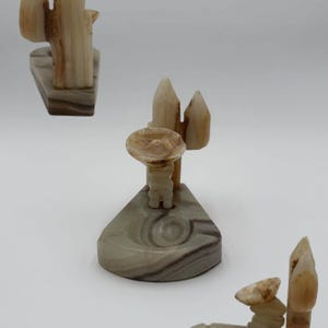 May include: Three carved onyx figurines. One depicts a cactus, another a man in a sombrero, and the third a man with a cactus. The figurines are in shades of beige, brown, and gray, with a polished finish. The bases are rectangular or triangular.