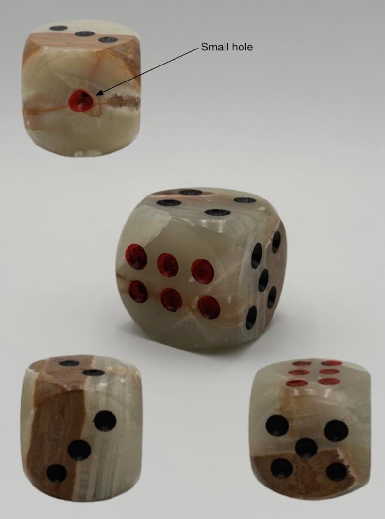 May include: A collection of stone dice with a marbled appearance. The dice have a light green and brown color scheme, with black and red dots indicating the numbers. The dice are shown from multiple angles.