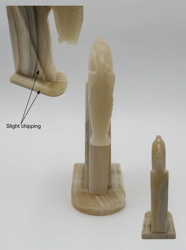 May include: A collection of beige and cream-colored onyx sculptures. The sculptures feature a stylized, abstract design with vertical and curved elements. One sculpture shows slight chipping. The pieces are displayed against a white background.