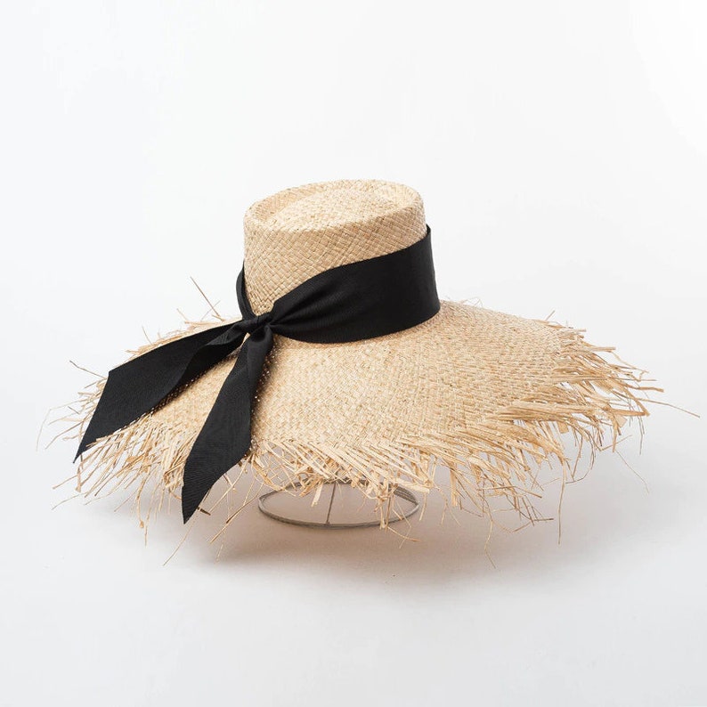 May include: A wide-brimmed straw hat with a black ribbon tied in a bow. The hat has a frayed edge and is made of natural straw.