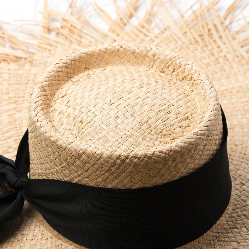 May include: A straw hat with a wide brim and a black ribbon around the crown.
