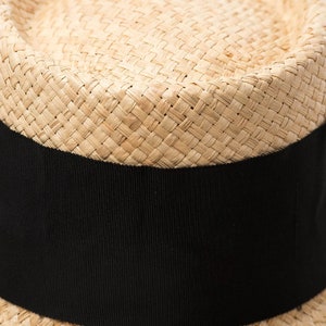 May include: A straw hat with a wide brim and a black ribbon band around the crown.