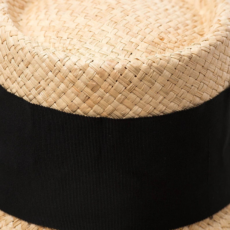 May include: A straw hat with a wide brim and a black ribbon band around the crown.