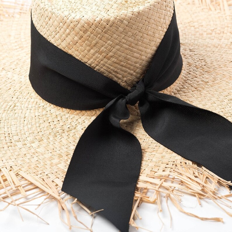 May include: A wide-brimmed straw hat with a black ribbon tied in a bow at the crown. The hat has a frayed edge and is made of natural straw.