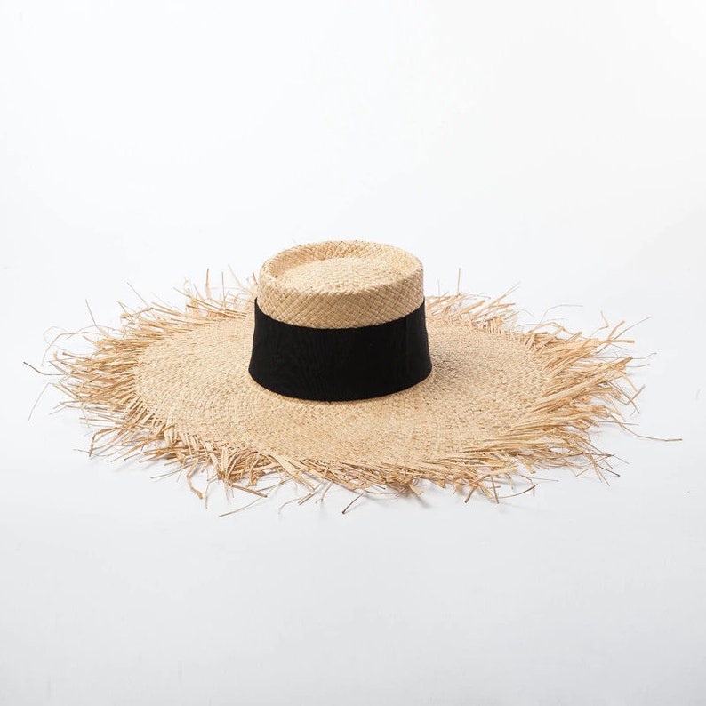 May include: A wide-brimmed straw hat with a black ribbon around the crown. The brim has a frayed edge.