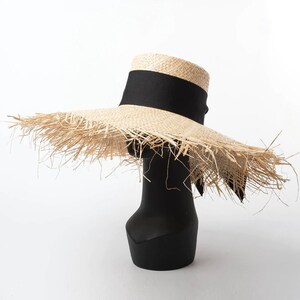 May include: A wide-brimmed straw hat with a black ribbon around the crown. The hat has a frayed edge and is sitting on a black mannequin.