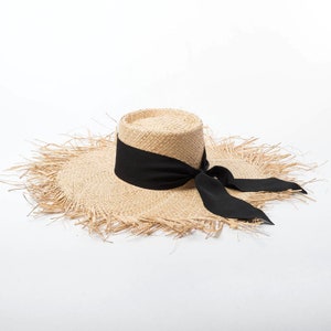 May include: A wide-brimmed straw hat with a black ribbon tied in a bow. The hat has a frayed edge and a flat crown.