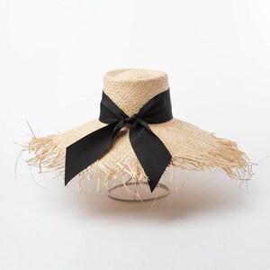May include: A wide-brimmed straw hat with a black ribbon tied in a bow. The hat has a frayed edge and is made of natural straw.