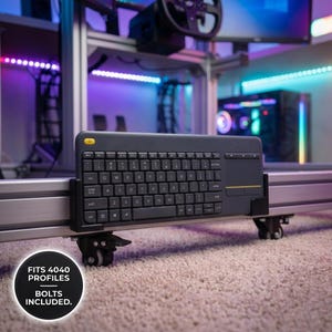 Può includere: Una tastiera nera con touchpad integrato è montata su un telaio metallico con ruote. La tastiera ha un pulsante giallo e lettere bianche. Il testo "FITS 4040 PROFILES BOLTS INCLUDED" è in un cerchio nero.