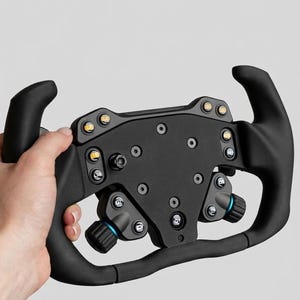 Può includere: Un volante da corsa nero con diversi pulsanti e manopole. Il volante ha un pannello di controllo centrale con diversi accenti gialli e blu. Le impugnature sono curve ed ergonomiche, progettate per una presa comoda durante il gioco.
