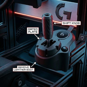 Puede incluir: Una palanca de cambios para juegos de color negro con pomo cilíndrico texturizado, placa de guía y base. Etiquetas de texto señalan SHIFT KNOB, GATED PLATE y REMOVE LEATHER BOOT, con el logotipo de la marca G visible en la unidad.