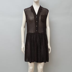 May include: A sleeveless, dark brown dress with a collared neckline and button-down front. The dress features a small pocket and a pleated skirt. The fabric has a subtle polka dot pattern. The dress is displayed on a mannequin.