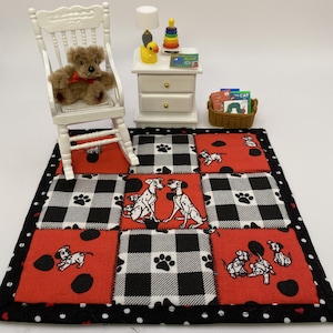 May include: Miniature dollhouse scene featuring a white chair with a teddy bear, a nightstand with a lamp and toys, and a patchwork rug with Dalmatian and paw print designs. The rug is red, black, and white.