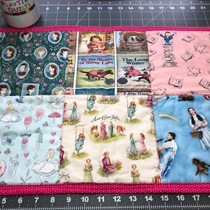 May include: A pink and white patchwork quilt with a pink border. The quilt is made up of different squares with various images, including a girl on a swing, a horse and rider, and a girl with a basket. The quilt is perfect for a child's room or a nursery.