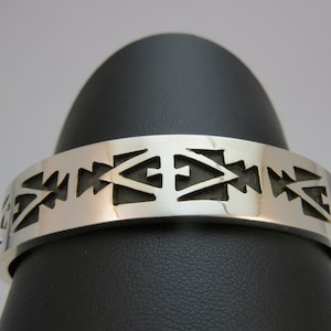 May include: A silver bracelet with a geometric pattern. The pattern is made up of triangles and squares, and it is repeated around the entire bracelet.