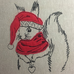 Può includere: Ricamo di uno scoiattolo che indossa un cappello da Babbo Natale rosso e una sciarpa, tenendo un cuore rosso nelle zampe.