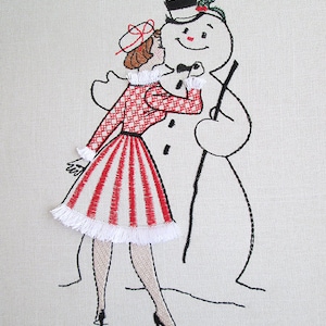Op de afbeelding: Geborduurde afbeelding van een vrouw in een rood-witte jurk die een sneeuwpop kust die een hoge hoed draagt en een stok vasthoudt.