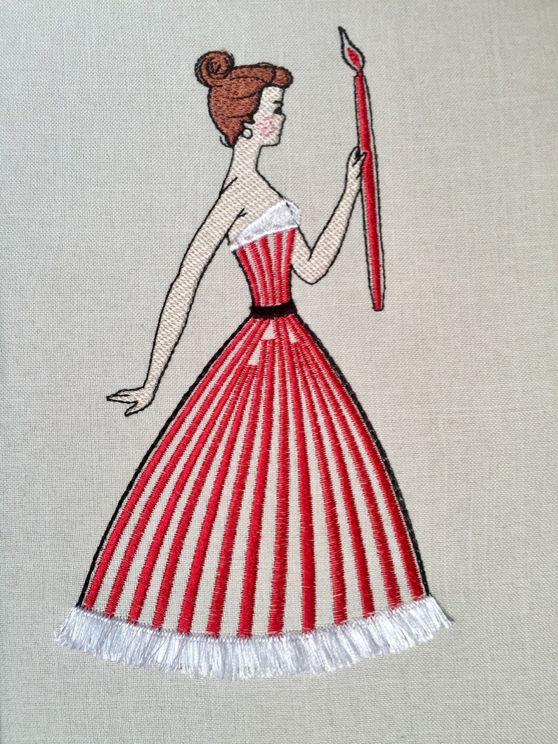 May include: Embroidered design of a woman in a red and white striped dress holding a red paintbrush. The dress has a white ruffle trim.