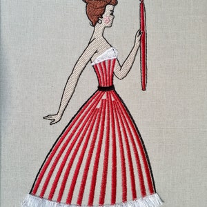 May include: Embroidered image of a woman in a red and white striped dress holding a red candle. The dress has a white fringe trim.