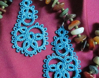 May include: A pair of blue crocheted earrings with a floral design. The earrings are hanging from a necklace made of brown, red, and green stones.