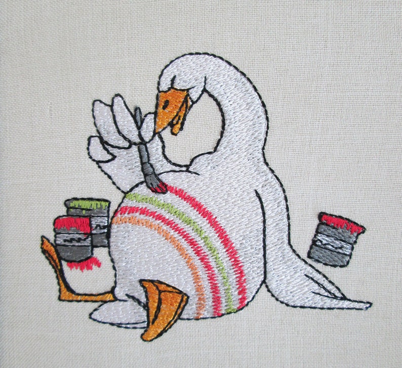 Op de afbeelding: Borduurwerk van een witte gans die zichzelf schildert met een kwast. De gans zit op zijn zij en heeft een regenboog van kleuren op zijn rug geschilderd. Er staan twee verfpotten naast de gans.