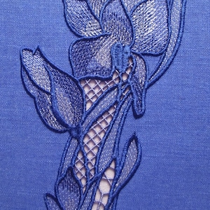 Könnte beinhalten: Blaue gestickte Blumenmuster auf einem blauen Leinenstoff. Das Design zeigt eine große Blume mit kleineren Blumen und Blättern.