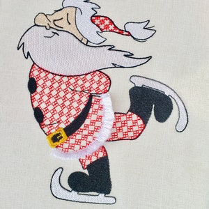 May include: Embroidered design of Santa Claus ice skating. He is wearing a red and white checkered suit with a white trim and a white beard. He has a black hat with a white pom-pom.