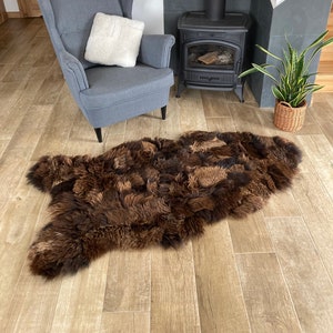 May include: A brown sheepskin rug with long, fluffy fur. The rug is laid out on a wooden floor in front of a fireplace.