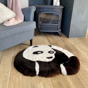 Może przedstawiać: Okrągły, czarno-biały dywan w kształcie pandy z puszystą fakturą. Dywan leży na drewnianej podłodze przed kominkiem.