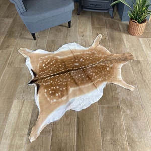 Könnte beinhalten: Ein brauner und weiß gefleckter Hirschfellteppich mit weißem Hintergrund. Der Teppich liegt auf einem Holzboden.