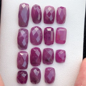 Puede incluir: Una colección de 14 piedras preciosas de rubí rosa facetadas, expuestas sobre un fondo blanco. Las piedras preciosas están dispuestas en filas y todas son aproximadamente del mismo tamaño y forma.