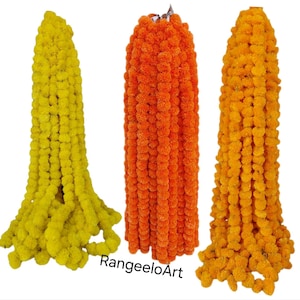 Puede incluir: Tres guirnaldas de caléndulas en tonos amarillo, naranja y dorado. Las guirnaldas están densamente repletas de pequeñas flores redondas, creando una exhibición texturizada y vibrante. Estas guirnaldas se utilizan probablemente para decoración o ceremonias religiosas.