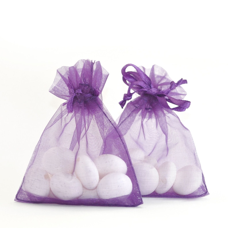 May include: Two purple organza bags filled with white candy. The bags have a drawstring closure and are tied with a purple ribbon.