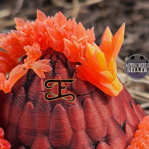 May include: A bright orange dragon figurine curled around a red dragon egg. The dragon has a crystal-like texture and is perched on top of the egg. The egg has a textured surface that resembles scales.