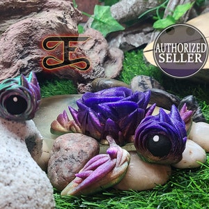 May include: An assortment of fantasy-themed, iridescent purple and green decorative objects. The objects are arranged on a bed of rocks and artificial grass. The image also includes the text "AUTHORIZED SELLER" in a circular badge.
