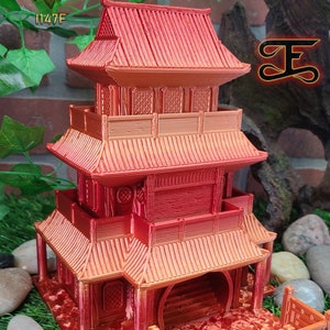May include: A multi-tiered, red and orange pagoda-style structure. The model features detailed roof lines, balconies, and a small fence. The text "MYTHIC ROLL" and "1147F" are visible. The structure is set on a bed of green grass.