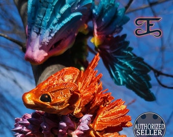 May include: Orange and purple 3D printed dragon figurine with wings perched on a tree branch. The dragon has a detailed textured surface and is surrounded by purple and pink flowers.