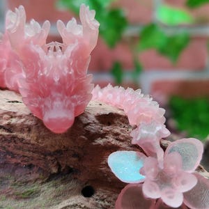 May include: A pink dragon figurine with a flower design. The dragon is made of a translucent material and has a detailed design. The flower is also made of a translucent material and has a delicate design.