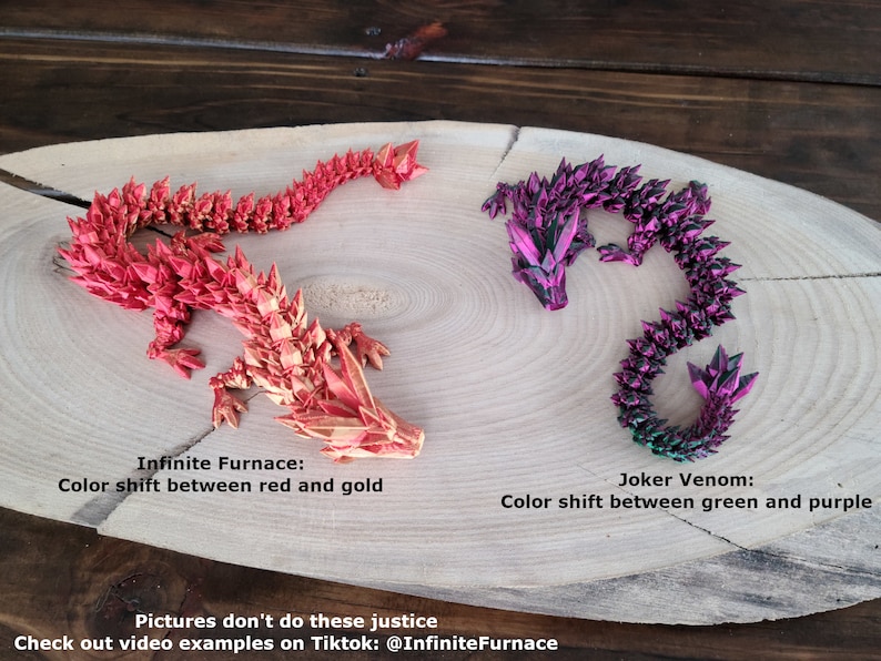 May include: Two origami dragons made of paper, one red and gold, the other green and purple. The dragons are on a wooden surface. The text "Infinite Furnace: Color shift between red and gold" is below the red dragon. The text "Joker Venom: Color shift between green and purple" is below the green dragon. The text "Pictures don't do these justice Check out video examples on Tiktok: @InfiniteFurnace" is at the bottom of the image.